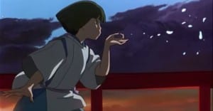 A young boy blows into his hand throwing out small pieces of paper off screen during the sunset